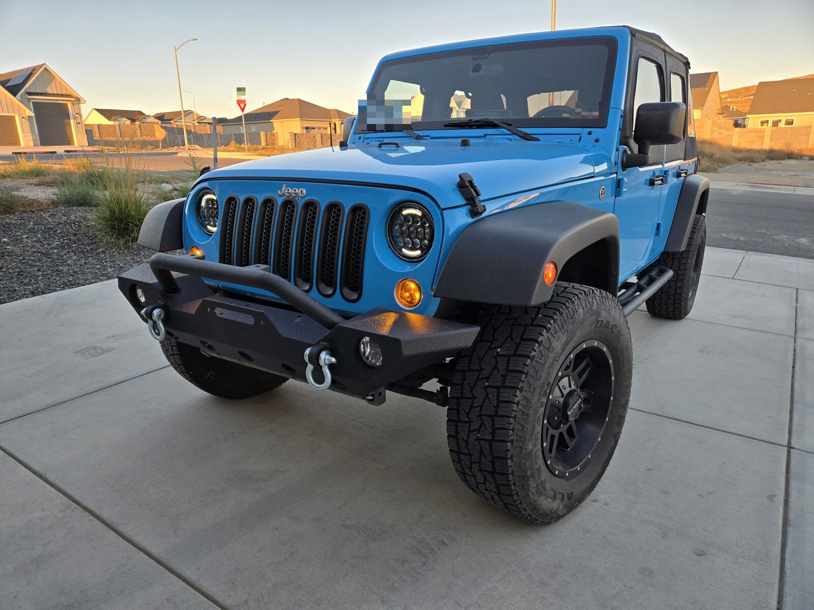 A lifted Jeep Wrangler Unlimited on 35-inch tyres with a steel front bumper, photographed from the front three-quarter in evening light.