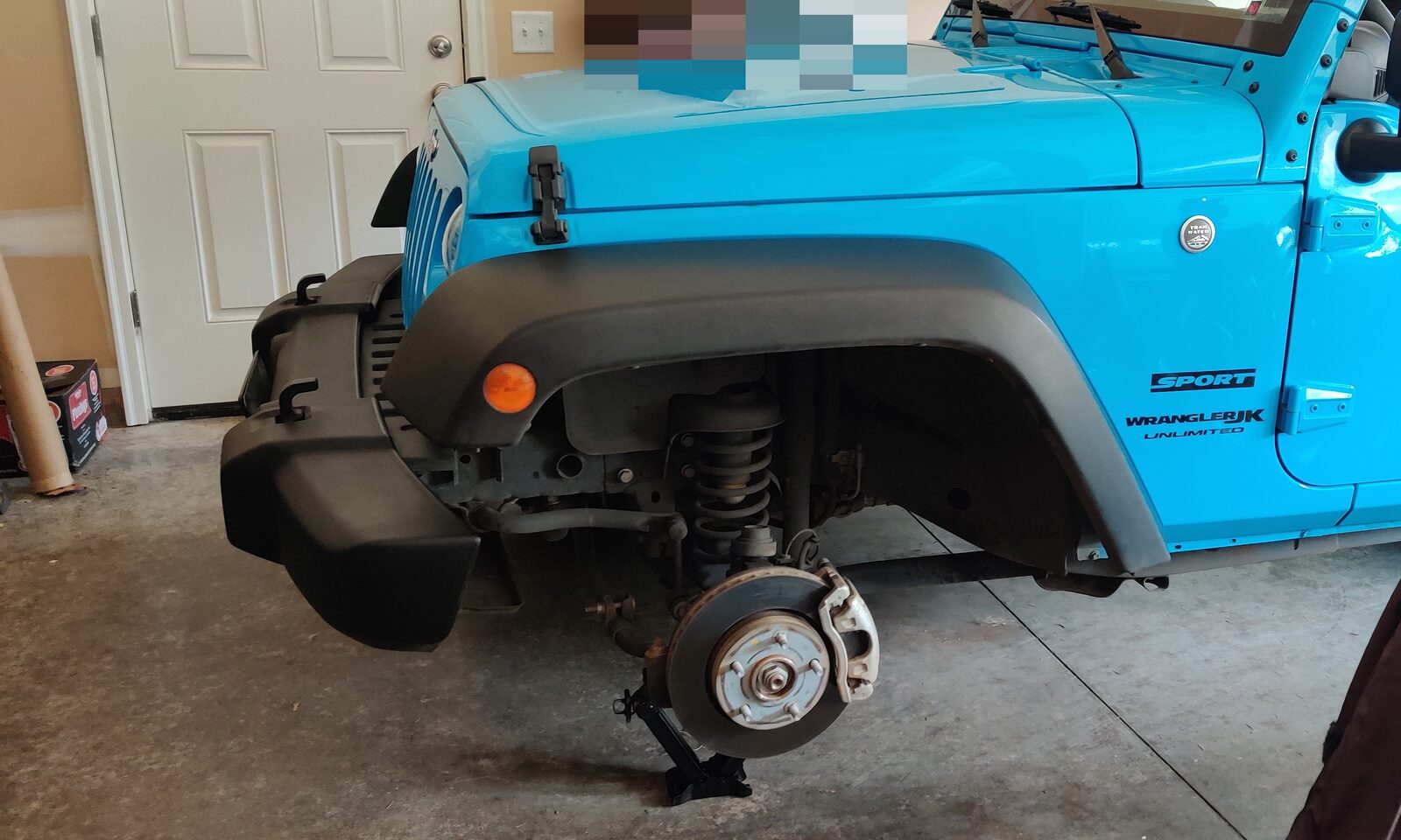 A Jeep in a garage with the front wheel removed, the brake rotor and hub bare and a bottle jack under the axle.