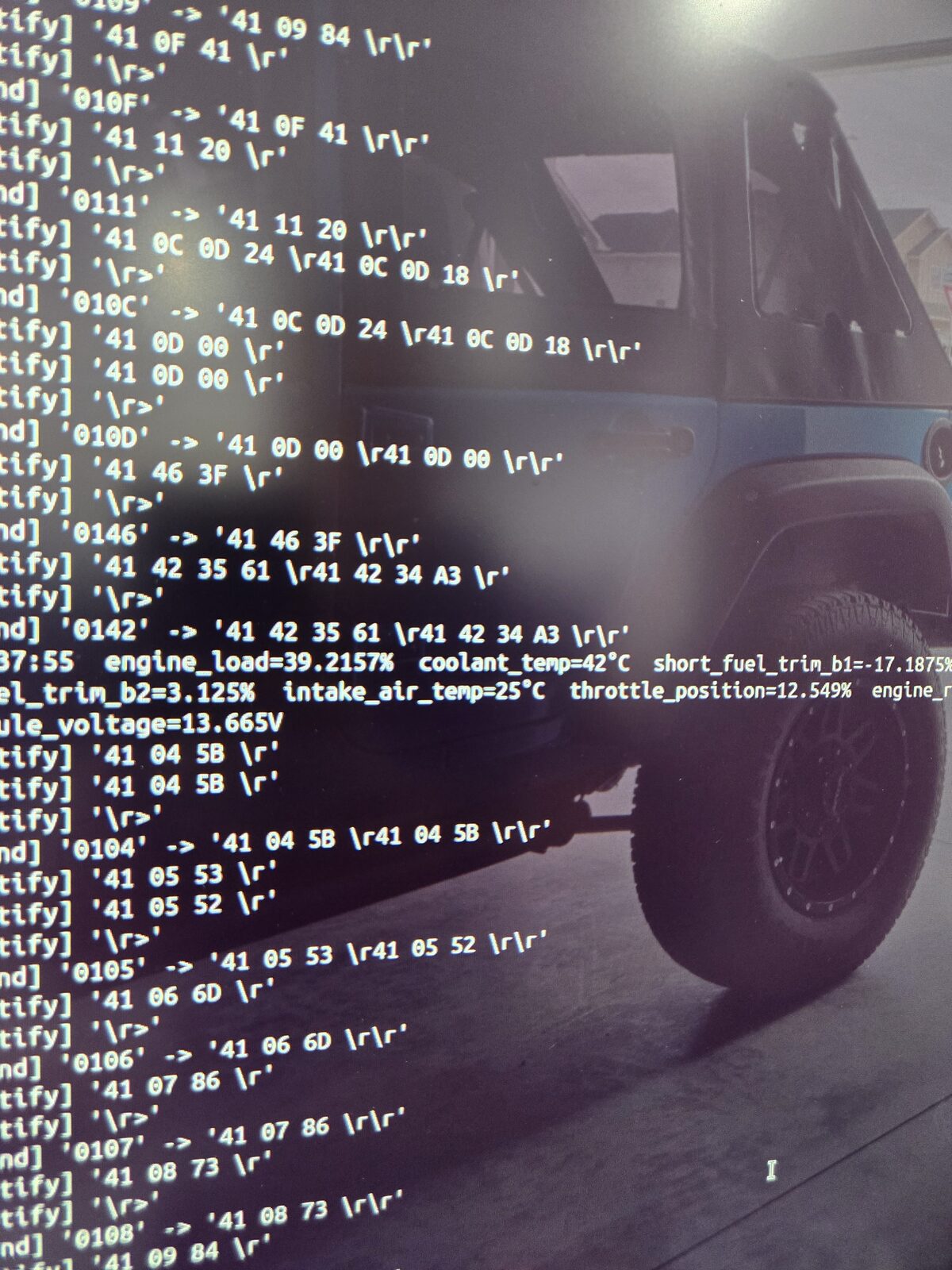 A phone held in front of an open engine bay, showing decoded engine values read from the vehicle.