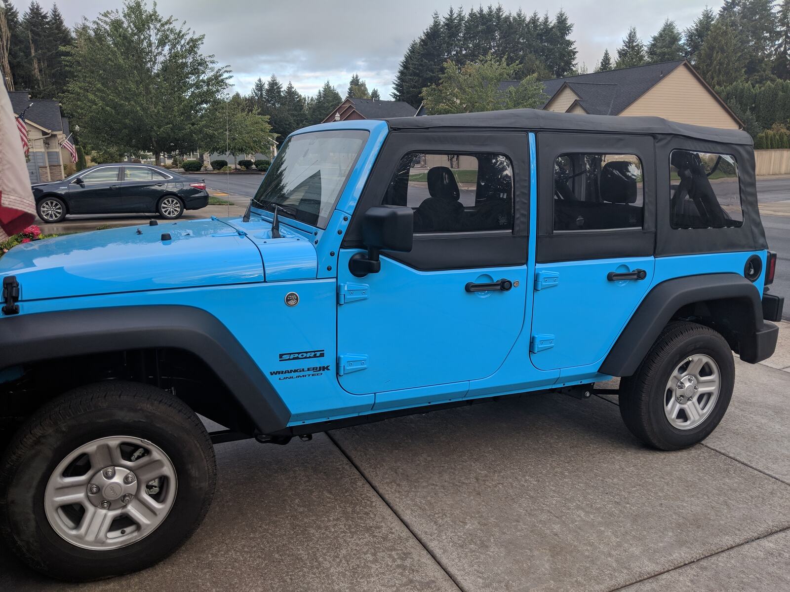 A blue Jeep Wrangler Unlimited on a driveway on an overcast morning, stock wheels, stock tyres, unlifted.